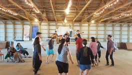 A small crowd at the John Arcand Fiddle Festival, gathered in front of a stage where three musicians are playing.