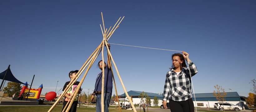 A photo of three people erecting a tipi.