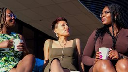 A photo of the directors of BIPOC Coffee Talk Inc. (Theresa Quagraine, Dyana Castillo, and Theodocia Quagraine) sitting together, holding mugs.