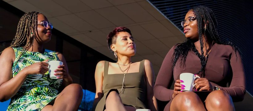 A photo of the directors of BIPOC Coffee Talk Inc. (Theresa Quagraine, Dyana Castillo, and Theodocia Quagraine) sitting together, holding mugs.