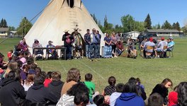 A photo of a person addressing a crowd of students at a pow wow.