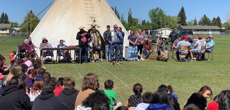 A photo of a person addressing a crowd of students at a pow wow.