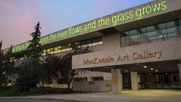 A photo of the entrance of the MacKenzie Art Gallery, with a neon green sign that reads “as long as the sun shines the river flows and the grass grows.”