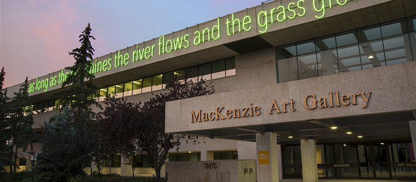 A photo of the entrance of the MacKenzie Art Gallery, with a neon green sign that reads “as long as the sun shines the river flows and the grass grows.”