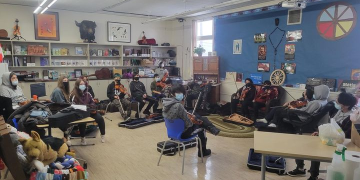 A photo of kids in a classroom learning to play the fiddle.