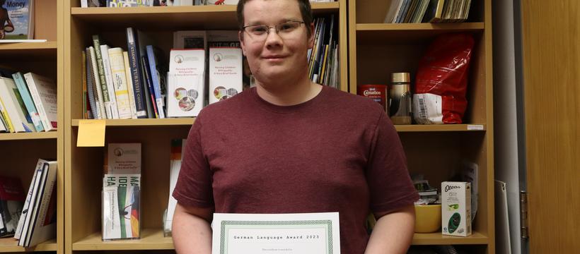 A photo of German language student Ethan holding up his award diploma.