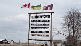 A photo of a sign that reads "The Log Cabin" in Redvers that offers tourist information.