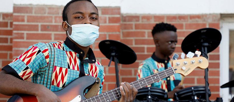 Two musicians playing the guitar and drums at the YWCA Re:Imagine Fashion event in 2021 for Culture Days. The one closest to the camera is wearing a face mask.