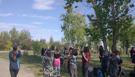 A photo of young students looking around them with binoculars in a park as part of the NatureHood Program.