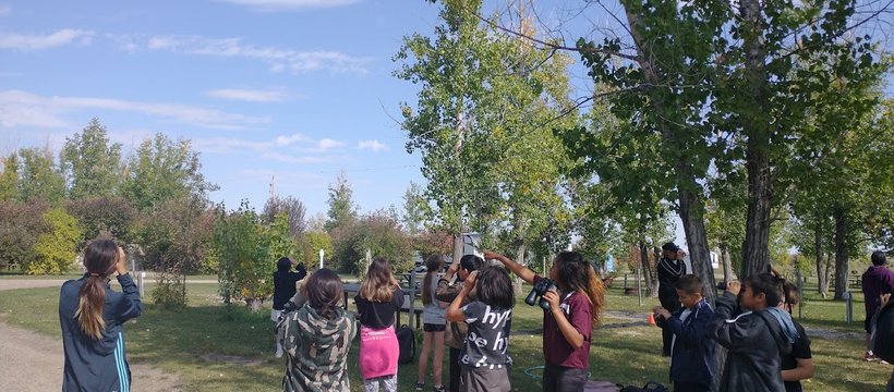 A photo of young students looking around them with binoculars in a park as part of the NatureHood Program.
