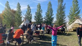 A photo of youth, smiling surrounded by nature and two tipis, at the culture camp on Muskoday First Nation.