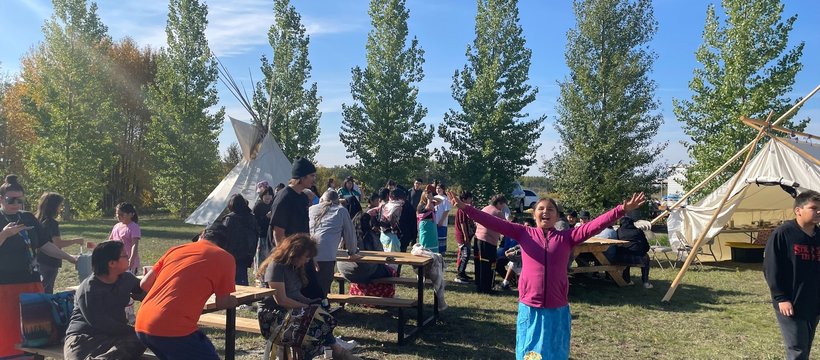 A photo of youth, smiling surrounded by nature and two tipis, at the culture camp on Muskoday First Nation.