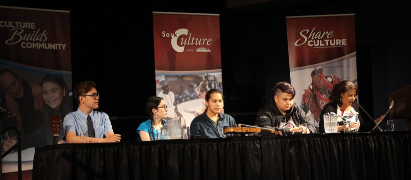 Five panelists sit at a table with SaskCulture banners behind them. 