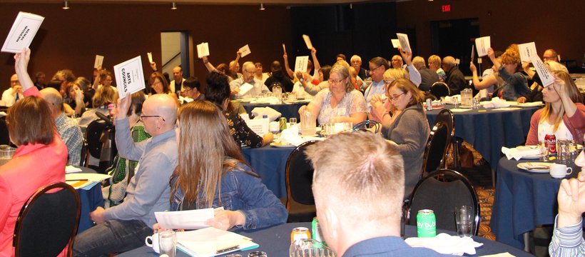 People at many tables hold up voting papers on a resolution.