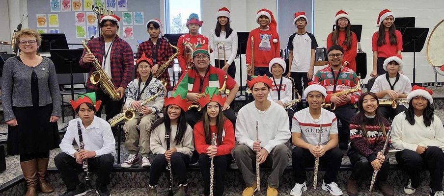 School band group photo with students in festive sweaters and Santa hats, holding instruments like saxophones, clarinets, and flutes.
