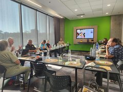 SaskCulture staff and board members sitting at tables around a screen discussion a presentation.