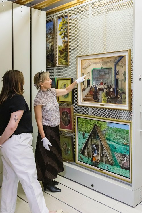 A photo of Dr. Jen Budney, Executive Director & CEO of the Ukrainian Museum of Canada, giving a tour of the collection and pointing out to one of the Kurelek's paintings.