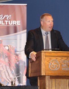 Minister Gene Makowski stands at a podium addressing the room.