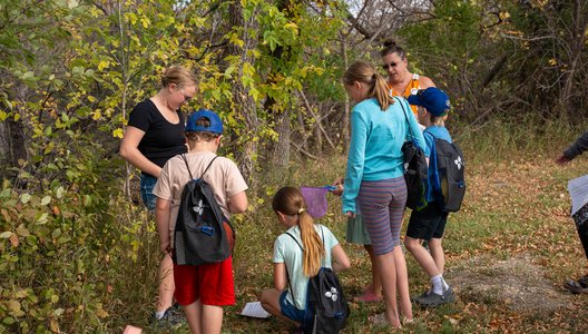 Group of children and volunteers looking at a page on the ground during a nature walk.