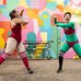 Two dancers move excitedly against a colourful mural on a building