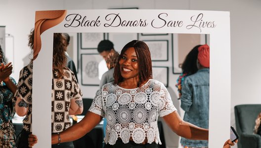 Person holding a large white photo frame prop with the text “Black Donors Save Lives” at the top.
