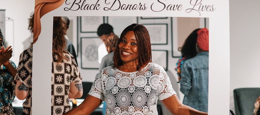 Person holding a large white photo frame prop with the text “Black Donors Save Lives” at the top.