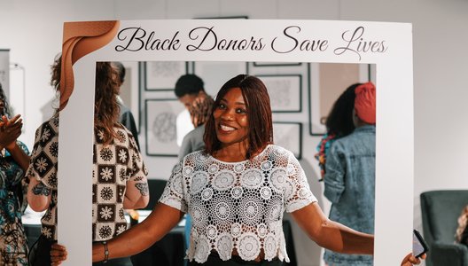 Person holding a large white photo frame prop with the text “Black Donors Save Lives” at the top.
