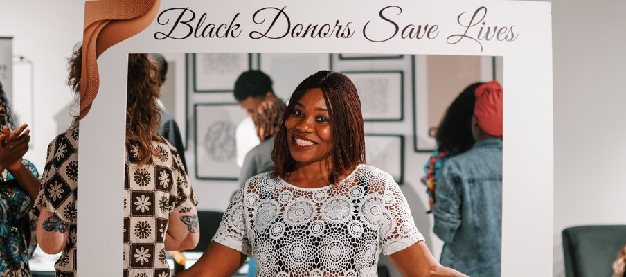 Person holding a large white photo frame prop with the text “Black Donors Save Lives” at the top.