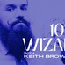 Bearded Magician Keith Brown holds a fan of playing cards near his face. He's seen from the chest up. The entire image is in blue. There is white text overlayed on top that says 100% Wizard with Keith Brown
