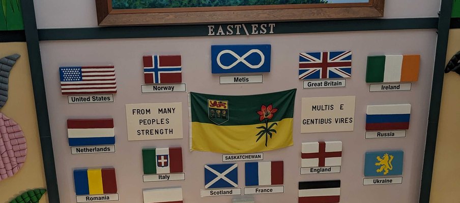 Exhibit wall featuring a framed painting of a bird flying over a winding river landscape at the top, with a display below showing various flags with languages to that the tours are offered in.
