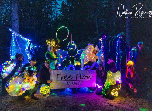 Dancers wearing glow in the dark costumes in a forested setting.
