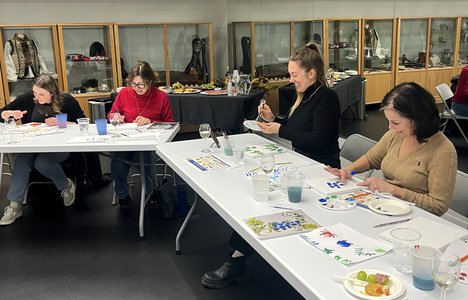 An image of participants sitting at the table and painting at one of Petrykivka & Wine Nights