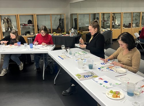 An image of participants sitting at the table and painting at one of Petrykivka & Wine Nights