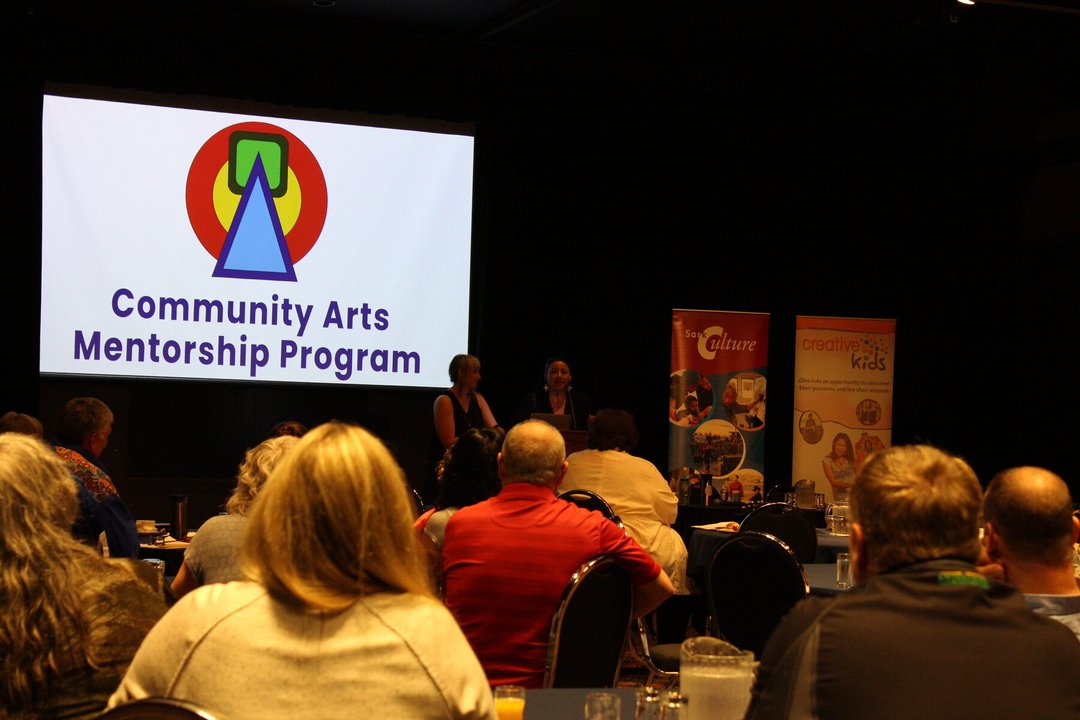 A photo of Eliza and Holly from CAMP speaking at the podium at the AGM, in front of a power point presentation.