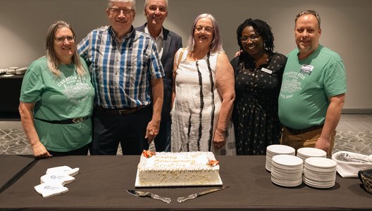 Group of people posing together in front of a cake.