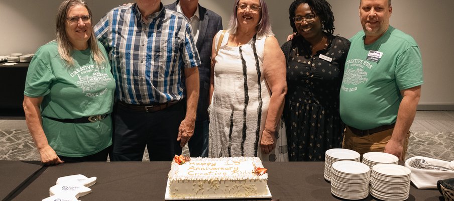 Group of people posing together in front of a cake.