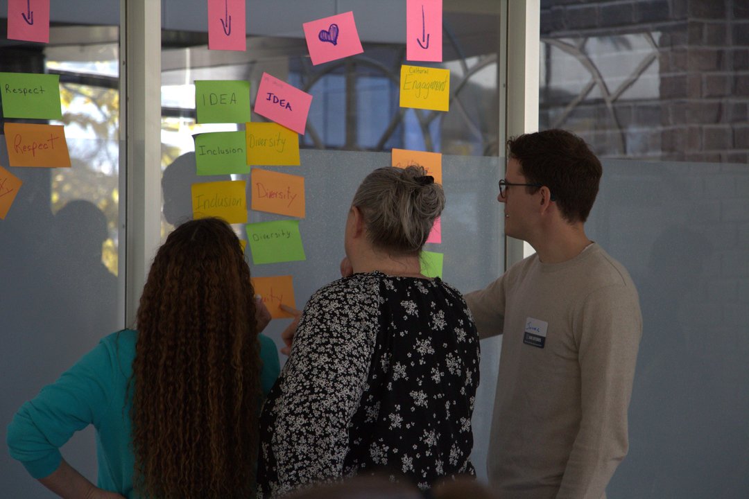 Three SaskCulture board and staff members look at a list of sticky notes during a exercise.