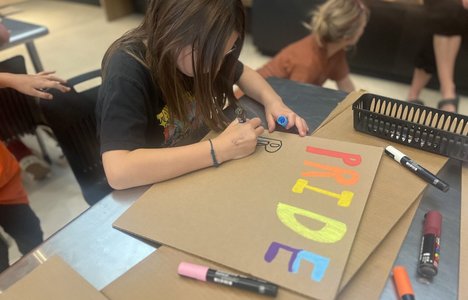 Youth participating in making pride signs using paint markers and cardboard.