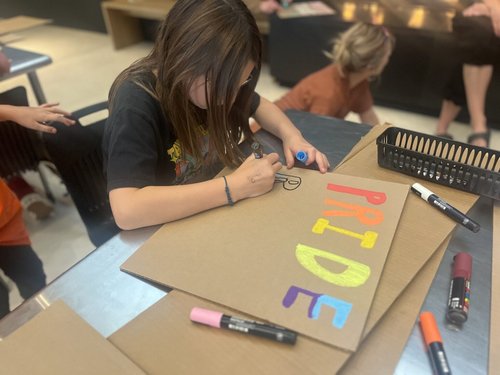 Youth participating in making pride signs using paint markers and cardboard.