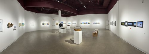 A panoramic image of a gallery space filled with paintings and sculptures made by community members.
