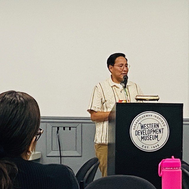 Person standing at a podium labeled “Western Development Museum” giving a presentation.