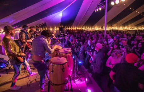 Photo of band preforming on the stage with a standing crowd listening