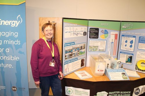 A smiling volunteer standing next to a Smarter Science Better Buildings workstation.