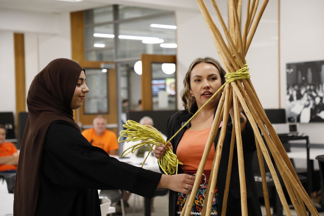 Two women raising a tipi together at an event