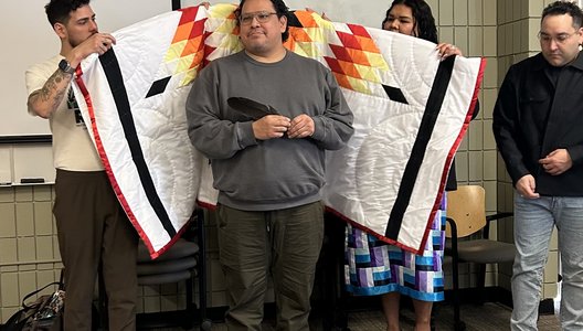 Photo of a Indigenous individual being wrapped in a star blanket.