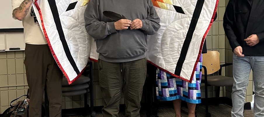 Photo of a Indigenous individual being wrapped in a star blanket.