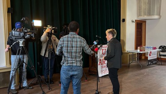 Photo of Em Ironstar being interviewed by a tv crew in front of a theater stage.