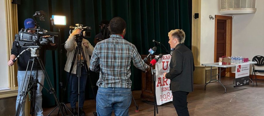 Photo of Em Ironstar being interviewed by a tv crew in front of a theater stage.