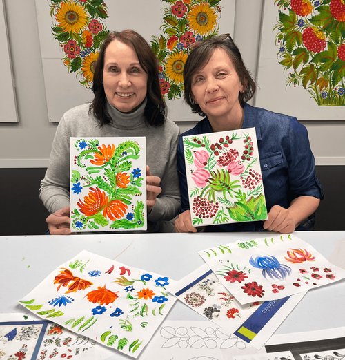 Photo of two workshop participants with their petrykivka paintings