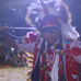 Still shot from the film with a Indigenous man dressed in traditional Indigenous dress dancing at a Powwoww..